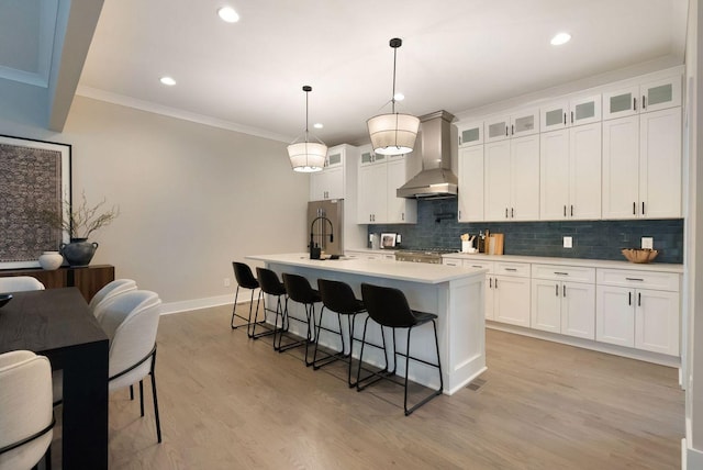 kitchen with crown molding, wall chimney exhaust hood, light countertops, backsplash, and a kitchen breakfast bar