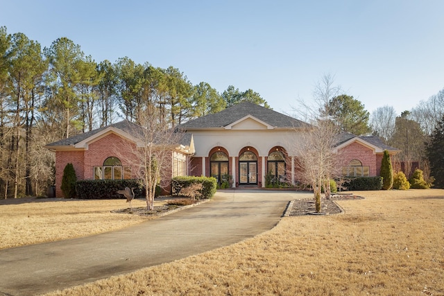 view of front of home featuring concrete driveway, brick siding, a front lawn, and french doors