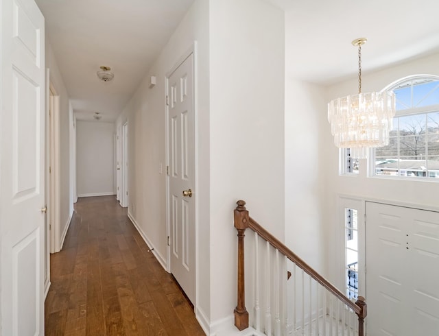 hallway featuring an inviting chandelier, baseboards, dark wood-type flooring, and an upstairs landing