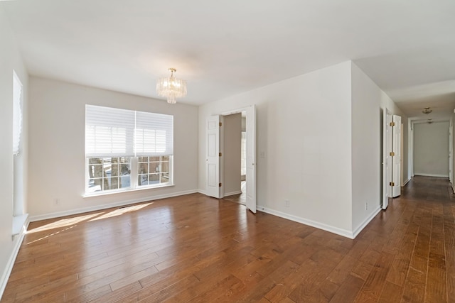 spare room with an inviting chandelier, baseboards, and hardwood / wood-style floors