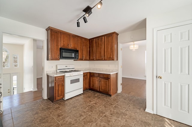 kitchen featuring black microwave, white gas stove, a chandelier, light countertops, and brown cabinetry