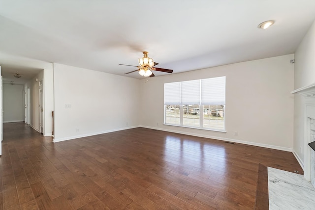 unfurnished living room featuring a ceiling fan, a fireplace, baseboards, and wood finished floors