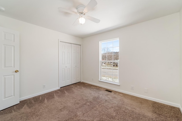 unfurnished bedroom featuring baseboards, visible vents, a ceiling fan, carpet floors, and a closet