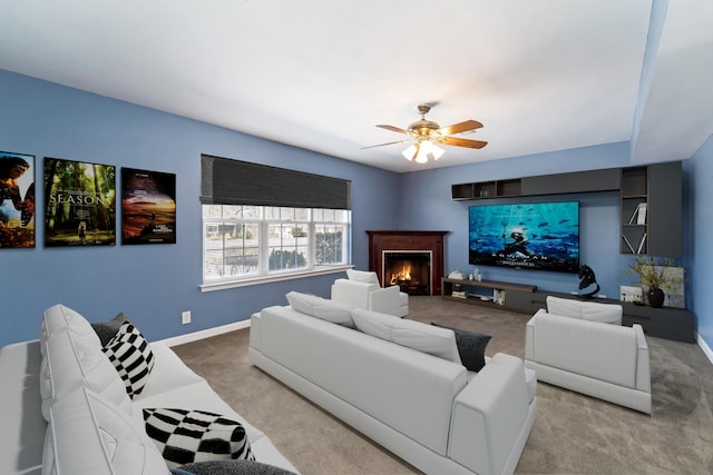 carpeted living room with a warm lit fireplace, ceiling fan, and baseboards