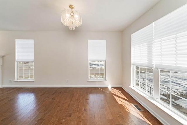 spare room featuring baseboards, hardwood / wood-style floors, visible vents, and a notable chandelier