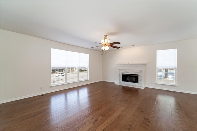 unfurnished living room featuring a ceiling fan, dark wood-style flooring, a healthy amount of sunlight, and a fireplace