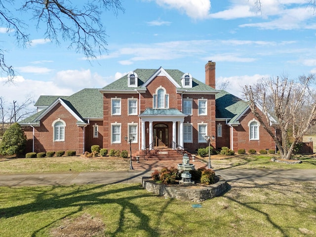 colonial house with brick siding, a chimney, and a front lawn