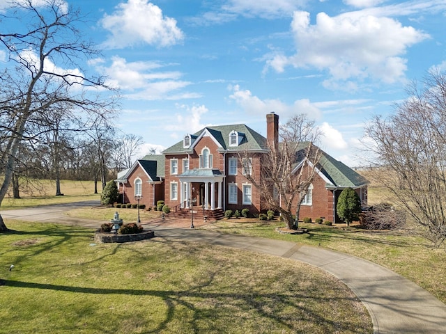 colonial home featuring driveway, brick siding, a chimney, and a front yard