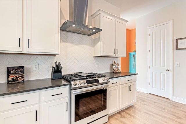 kitchen with wall chimney range hood, stainless steel gas range, light wood finished floors, dark countertops, and tasteful backsplash