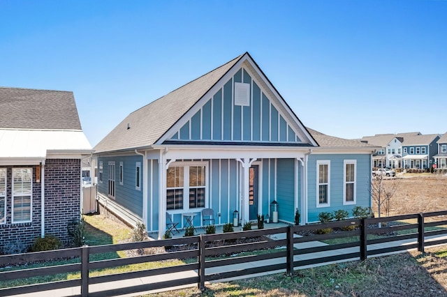 view of front of home with covered porch, a shingled roof, board and batten siding, and a fenced front yard