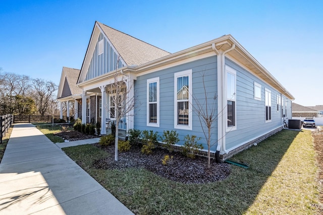 view of side of home with central AC, a yard, roof with shingles, and fence