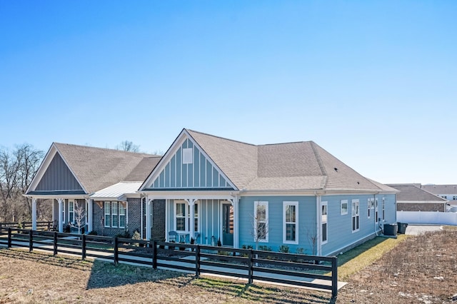 view of front facade with board and batten siding, a shingled roof, a fenced front yard, and central AC unit