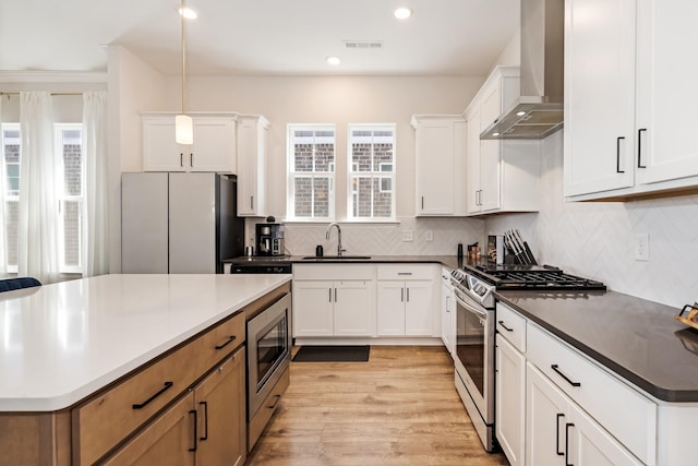 kitchen with visible vents, backsplash, appliances with stainless steel finishes, a sink, and wall chimney range hood