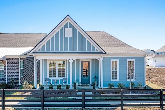 view of front of home featuring covered porch, brick siding, roof with shingles, and a fenced front yard