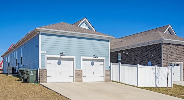 view of home's exterior featuring brick siding, central air condition unit, concrete driveway, fence, and a garage