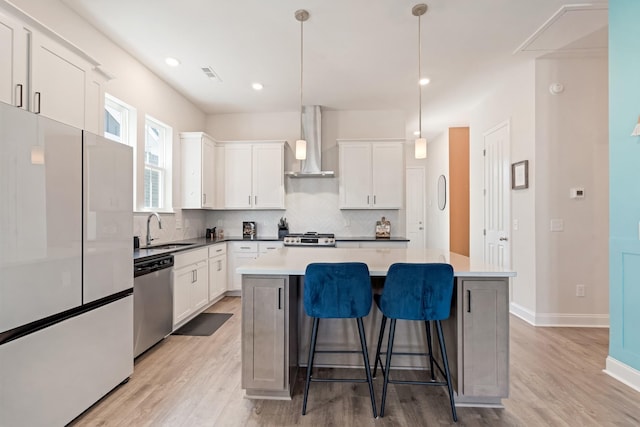 kitchen featuring visible vents, a kitchen island, freestanding refrigerator, wall chimney range hood, and stainless steel dishwasher