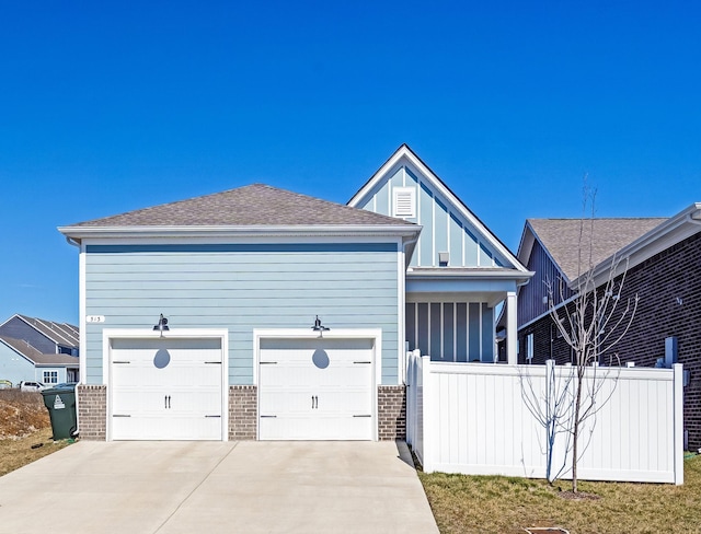 view of front of property with a shingled roof, brick siding, driveway, and fence