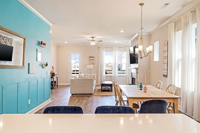 dining room featuring a healthy amount of sunlight, wood finished floors, visible vents, and crown molding