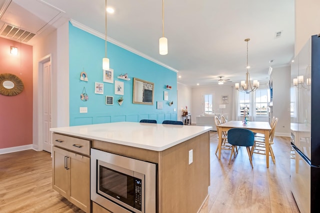 kitchen featuring light wood-style flooring, a kitchen island, stainless steel microwave, and ornamental molding