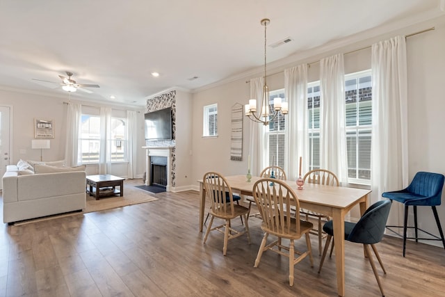 dining space with visible vents, ornamental molding, a fireplace with flush hearth, wood finished floors, and ceiling fan with notable chandelier