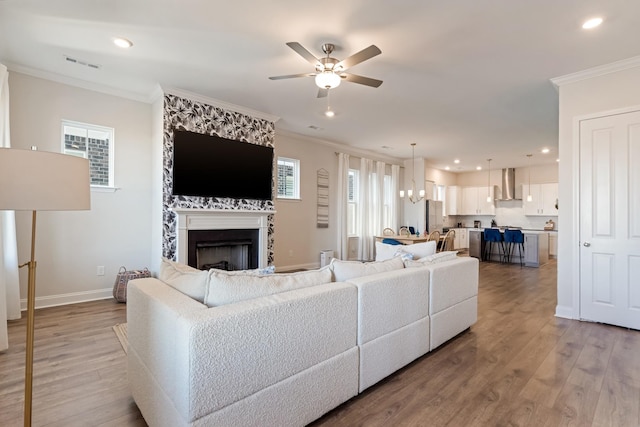 living room with light wood-style flooring, a fireplace, visible vents, baseboards, and ornamental molding