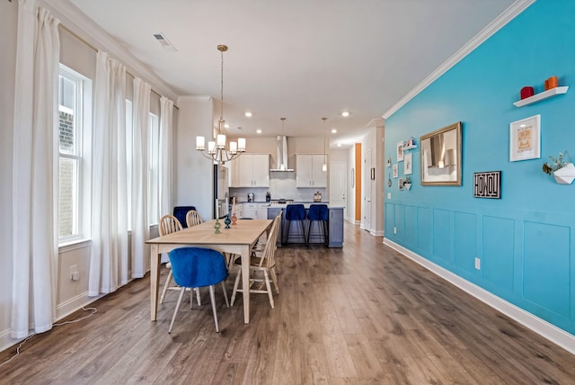 dining room featuring a chandelier, a decorative wall, dark wood-type flooring, visible vents, and ornamental molding