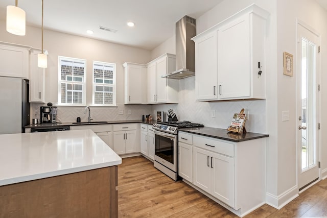 kitchen featuring a sink, wall chimney range hood, appliances with stainless steel finishes, light wood finished floors, and tasteful backsplash