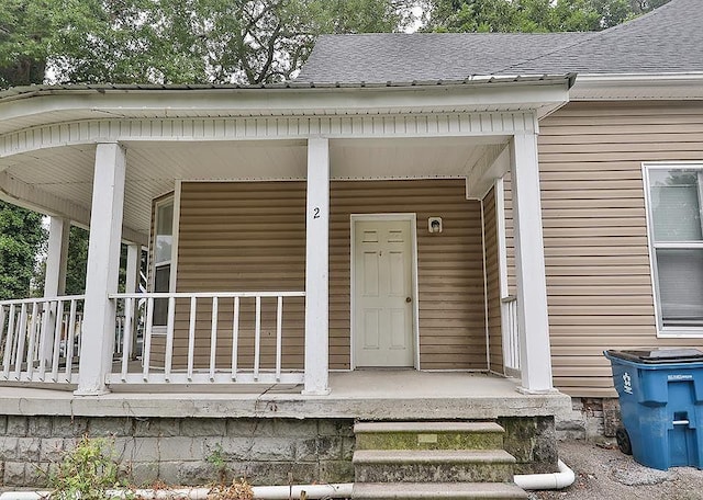 doorway to property with covered porch and a shingled roof