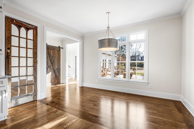 unfurnished dining area with baseboards, a barn door, wood finished floors, and crown molding