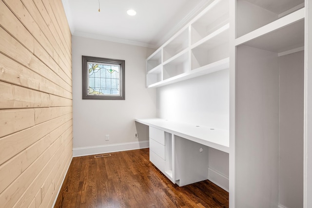 unfurnished office featuring crown molding, built in desk, visible vents, dark wood-type flooring, and baseboards