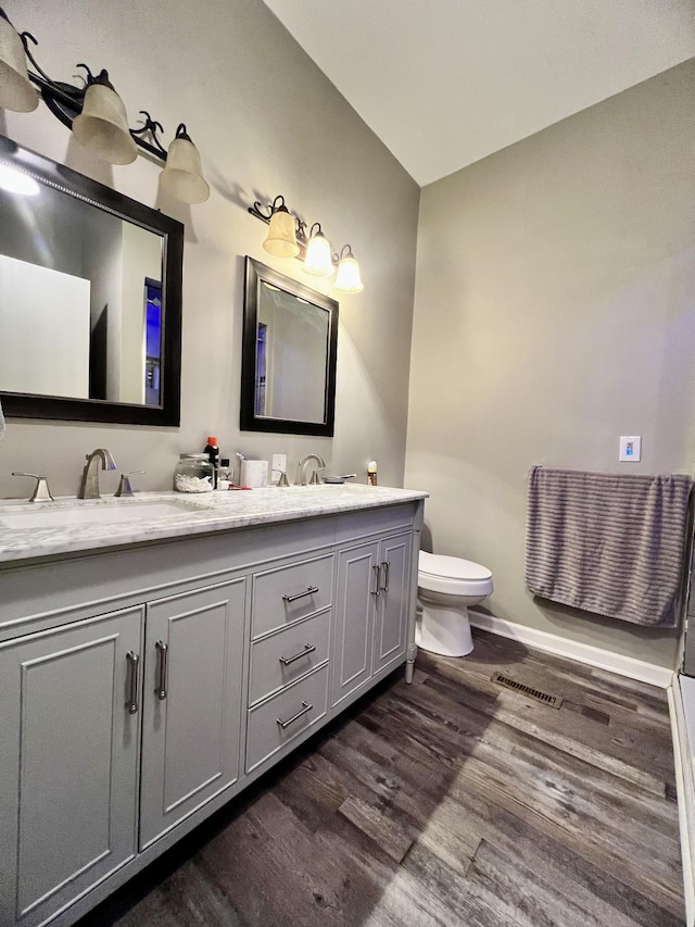 bathroom featuring double vanity, visible vents, toilet, wood finished floors, and baseboards