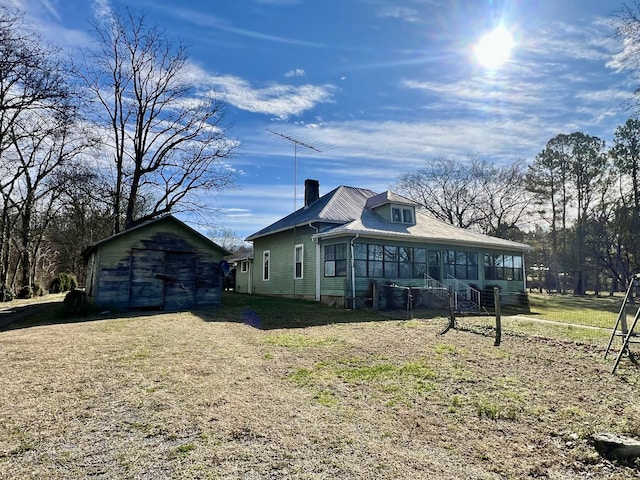 view of property exterior with a lawn, a chimney, an outdoor structure, and a sunroom