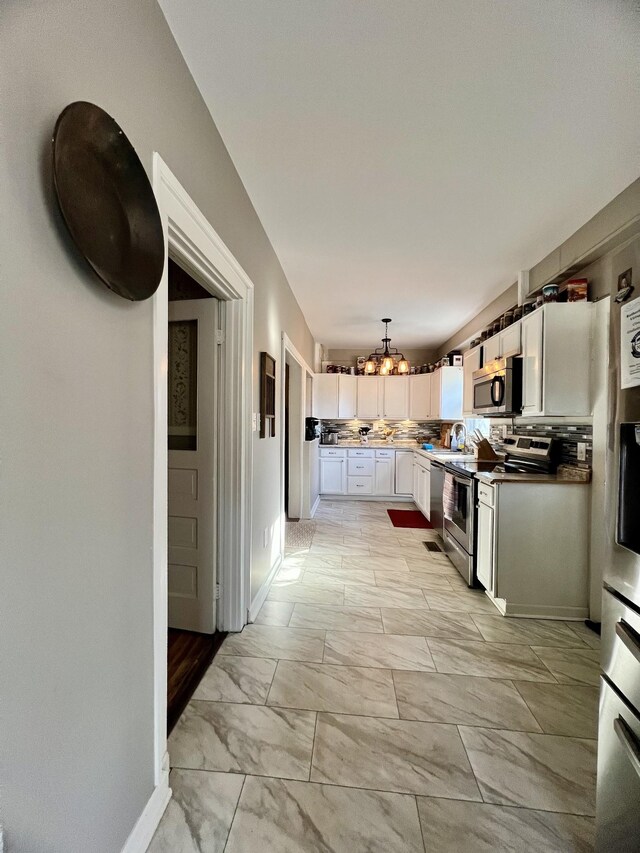 kitchen with decorative light fixtures, an inviting chandelier, marble finish floor, stainless steel appliances, and white cabinetry