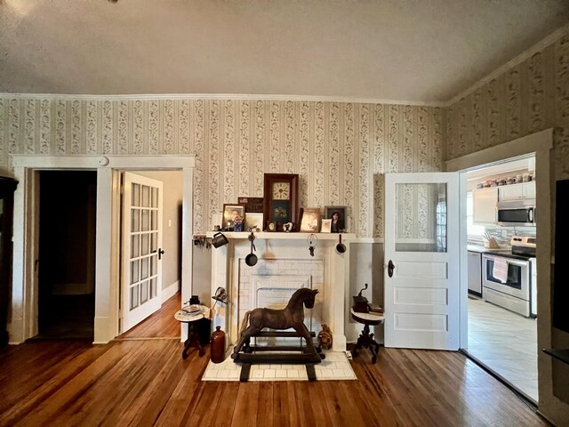 sitting room with wallpapered walls, a fireplace, ornamental molding, and wood finished floors