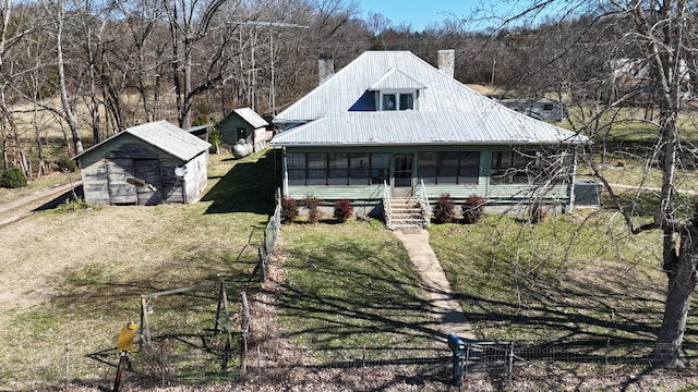 view of front facade featuring metal roof, an outdoor structure, a sunroom, a shed, and a front yard