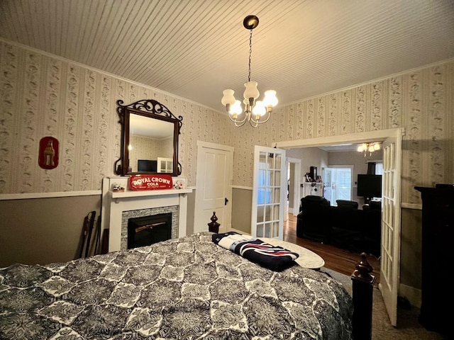 bedroom with wallpapered walls, wood finished floors, crown molding, a fireplace, and a chandelier