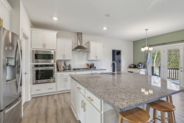 kitchen featuring a sink, white cabinetry, appliances with stainless steel finishes, decorative backsplash, and wall chimney exhaust hood