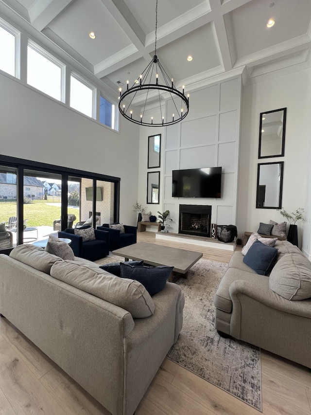 living area featuring a high ceiling, a fireplace, light wood-style flooring, and an inviting chandelier