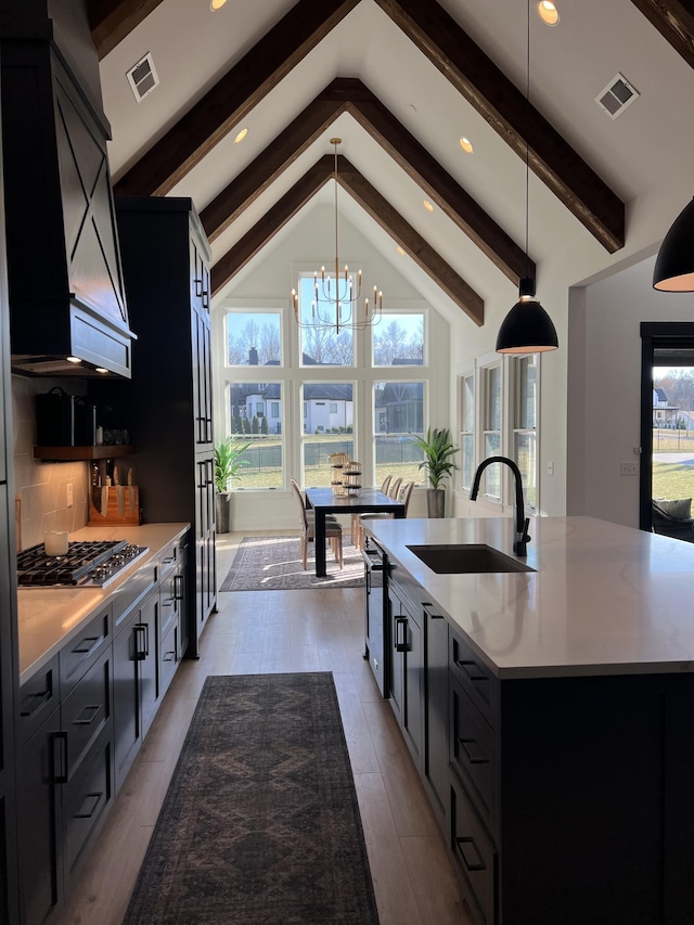 kitchen featuring stainless steel gas cooktop, tasteful backsplash, visible vents, a sink, and dark cabinets