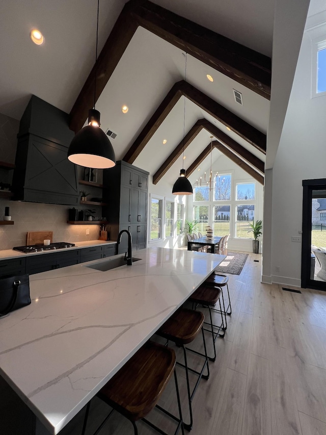 kitchen with visible vents, light stone counters, beamed ceiling, stainless steel gas cooktop, and a sink