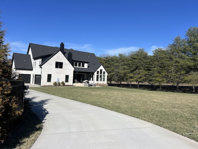 rear view of property featuring a garage, a yard, a chimney, and driveway