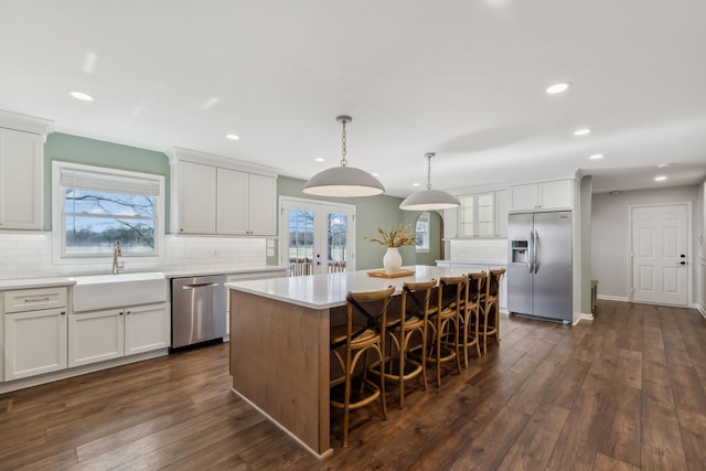 kitchen with dark wood-style floors, stainless steel appliances, light countertops, a sink, and a kitchen island