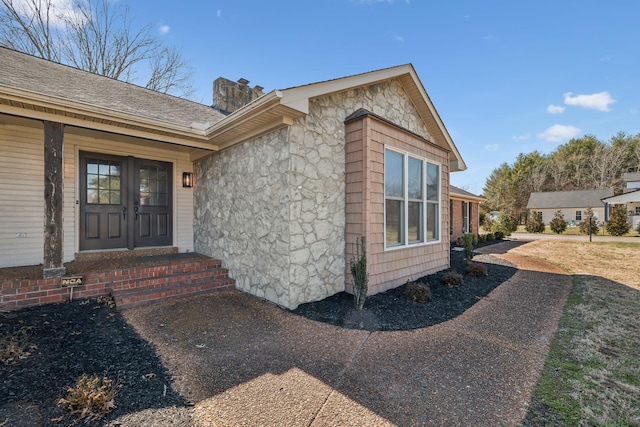 entrance to property featuring stone siding, roof with shingles, and a chimney