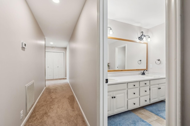 corridor with light tile patterned flooring, light colored carpet, a sink, visible vents, and baseboards