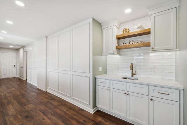 bar with dark wood-style flooring, a sink, backsplash, and recessed lighting