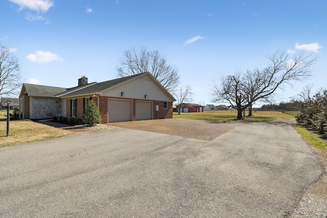 view of property exterior featuring a yard, brick siding, a chimney, and aphalt driveway