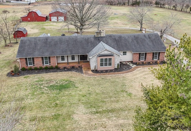 view of front facade with an outbuilding, roof with shingles, a barn, a front lawn, and a chimney
