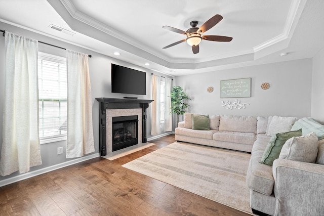 living area with a wealth of natural light, wood-type flooring, visible vents, and a tray ceiling