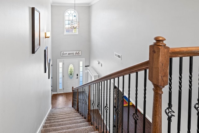 stairs with crown molding, visible vents, a towering ceiling, an inviting chandelier, and baseboards