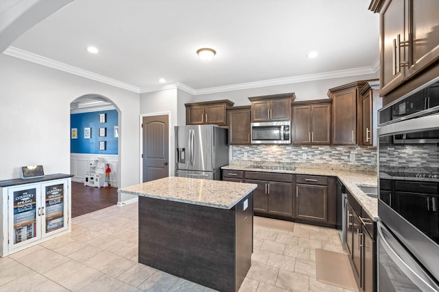 kitchen featuring arched walkways, a kitchen island, light stone counters, appliances with stainless steel finishes, and dark brown cabinets